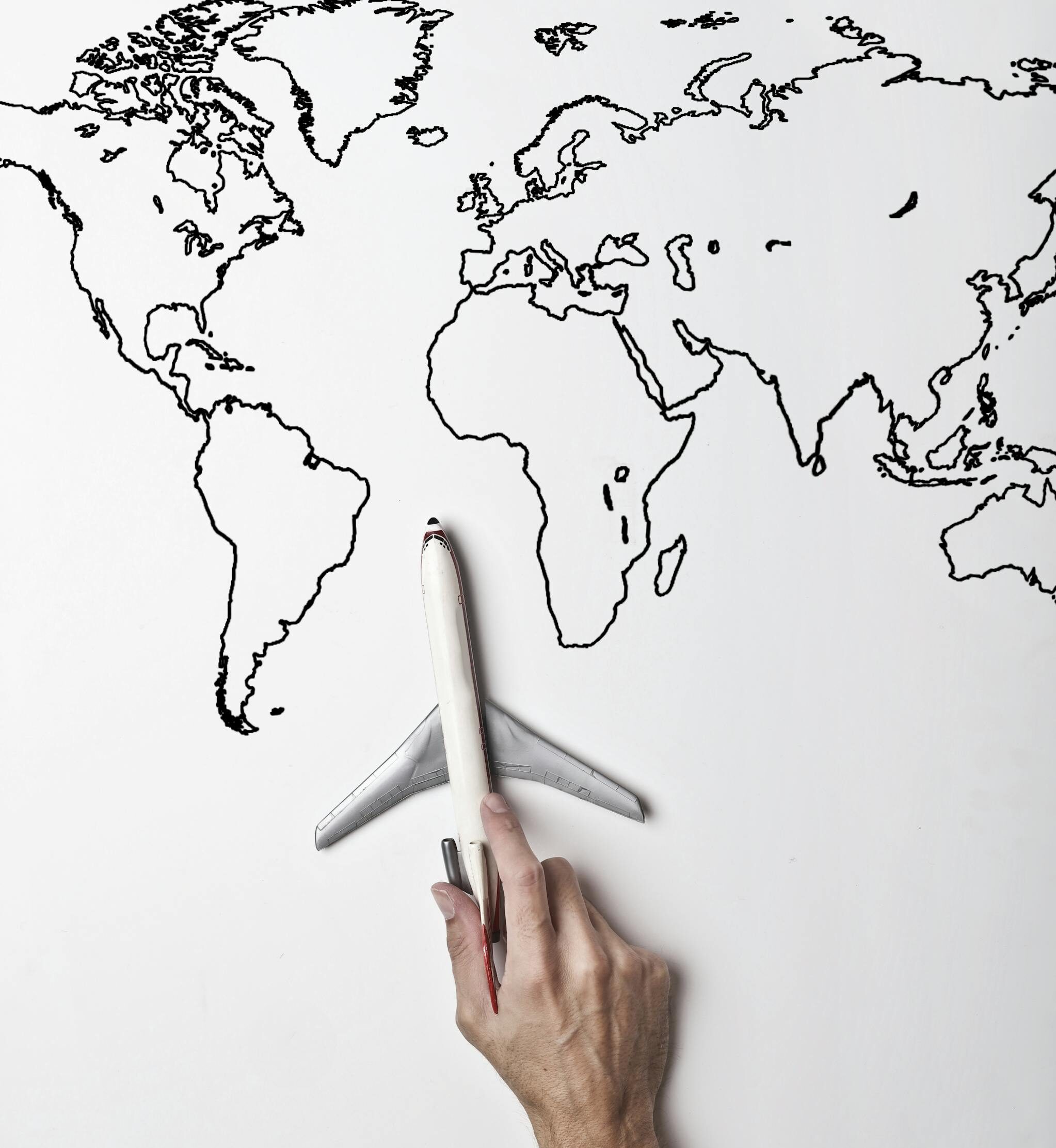 Crop person in vibrant yellow clothes holding little gray plane against contour map on white wall as concept of tourism and adventure